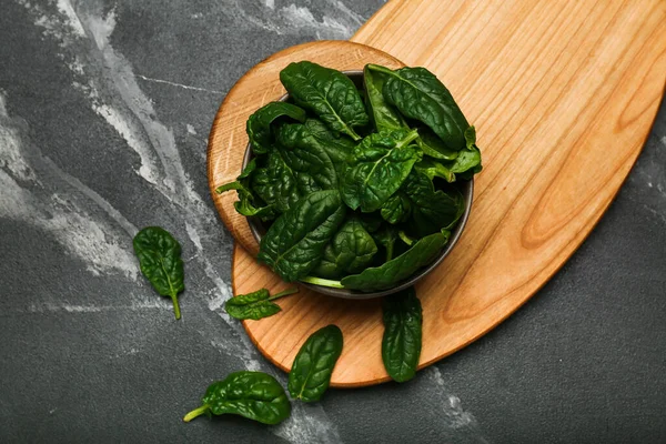 Organic food concept with spinach leaves in bowl on black background top view