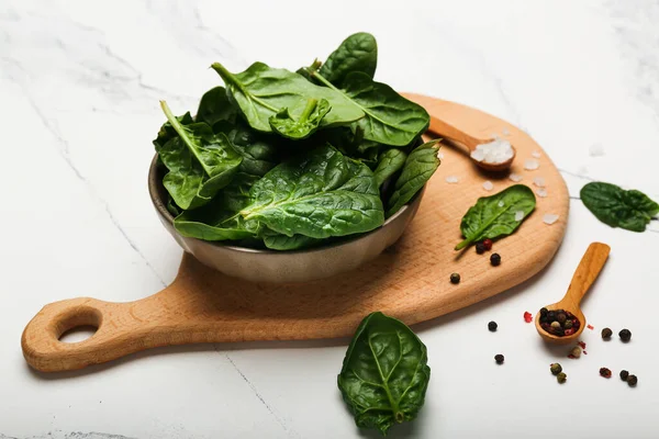 spinach in a bowl on a wooden cutting board with pepper and salt. White background