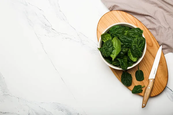 spinach leaves in a bowl on a cutting board with a knife on a white background top view. White background