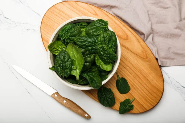 spinach leaves in a bowl on a cutting board with a knife on a white background top view. White background