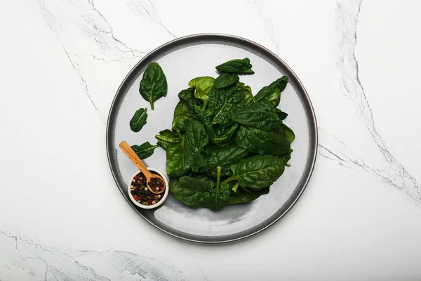 Organic food concept with spinach leaves on a plate with pepper top view closeup. White background