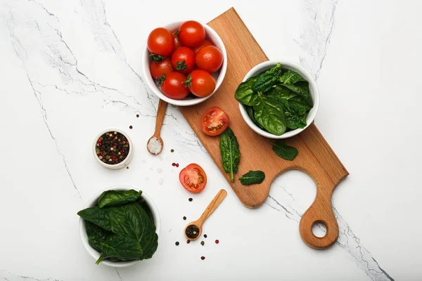 tomatoes with spinach in a bowl on a wooden cutting board with peppers. White background, top view