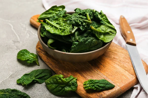 Organic food concept with spinach leaves in a bowl on a cutting board with a knife on a gray background