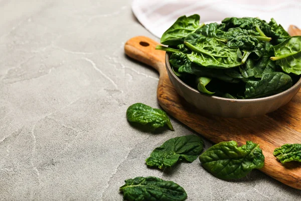 Organic food concept with spinach leaves in a bowl on a cutting board with a knife on a gray background