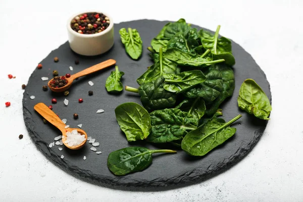 spinach leaves on a stone cutting board with wooden spoons with salt and pepper on a white background