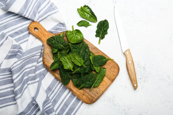 cutting board with spinach leaves and a knife on a napkin on a white background top view