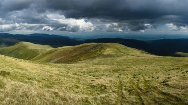 Capatanii Massif 'in tepesindeki güneşli bir çayırın üzerindeki karanlık, fırtınalı bulutlar. Haziran, Carpathia, Romanya.