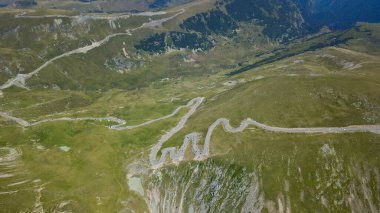 Transalpina yolunun hava aracı panoraması keskin dağ zirveleri boyunca kıvrılıyor ve dik bir uçurumun yanında. Parang Dağları 'nın dağları turistlerle doludur. Carpathia, Romanya