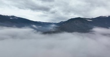 Yavaşça bulutların üzerinden drone atışı. Bir dağın etrafında dönüyor..