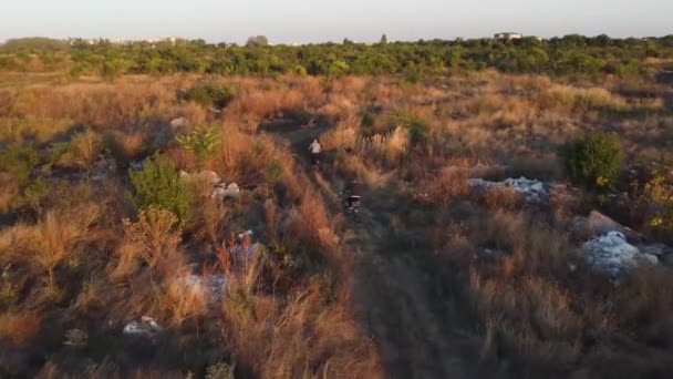 Aerial view of 2 bikers riding a path full of waste garbage land close to a city — Vídeos de Stock