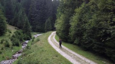 Genç adam yaz mevsiminde nehrin yanındaki patikada uzun ağaçların arasında yürüyor.