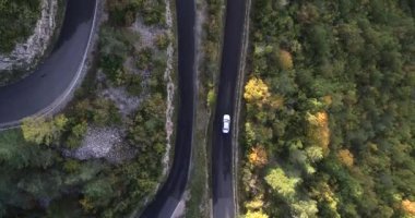 Havadan aşağıya, beyaz araba asfalt bir yoldan dağa doğru gidiyor. Yüksek kaliteli 4K DJI Phantom 4 PRO İHA görüntüsü Haziran 2020 'de çekildi