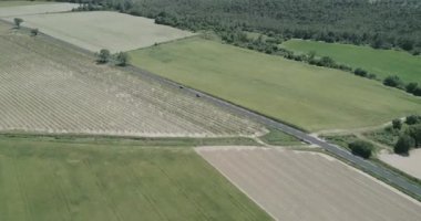 Yeşil tarlalar ve kuru, tepeler, bitkiler ve dağlarla çevrili. Bir araba geçiyor. Yüksek kaliteli 4K DJI Phantom 4 PRO görüntüleri Mayıs 2020 'de Güney Fransa' da çekildi