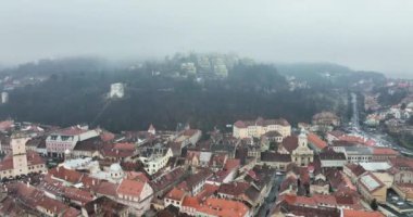 Sisli bir sabah Brasov şehrinde uçuyoruz. Ortaçağ şehrinin sonbahar manzarası. Yüksek kaliteli DJI Mavic 34k 5.1 K görüntü Kasım 2021. Güçlendirilmiş Ortaçağ Kalesi. Konsey Eski Meydanı
