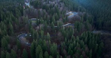 Aerial top-down drone shot above the winding mountain road close to sunset. Cars and trucks passing. High-quality DJI Mavic 3 4k 5.1k cinematic footage filmed in January 2022 in Brasov, Romania