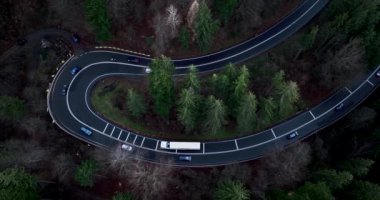 Aerial top-down drone shot above the winding mountain road close to sunset. Cars and trucks passing. High-quality DJI Mavic 3 4k 5.1k cinematic footage filmed in January 2022 in Brasov, Romania
