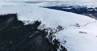 A dense evergreen spruce forest covers the white snow-capped hills. High-quality DJI Mavic 3 5.1k and 4k footage were made in January 2022 in Romania on a sunny cold day.