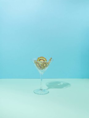 Durgun hayatın modern kavramsal ortamı. Kokteyl bardağında kurutulmuş meyve. Arka planda iki ton mavi ve yeşil kivi..