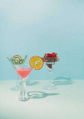 Durgun hayatın modern kavramsal ortamı. Kokteyl bardağında meyve. Taze çilek ve kurutulmuş kivi. Arka planda mavinin iki tonu.