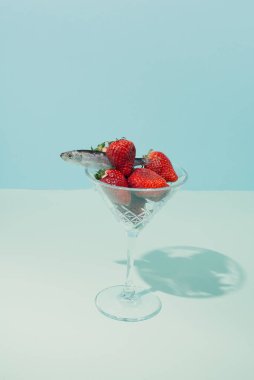 Durgun hayatın modern kavramsal ortamı. Bardakta balık ve çilek. Pastel mavi arkaplan.