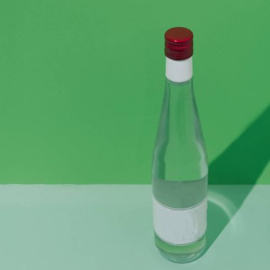 Yeşil arka planda bir şişe. Kırmızı kepenk. Boş etiket. Kavramsal ortam, minimalizm.