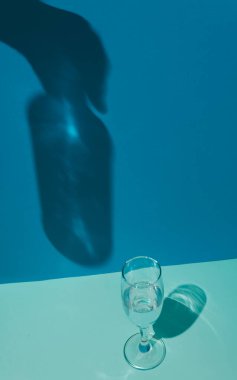 Mavi ayarı olan bir bardakta şampanya ve elinde şişe tutan bir el gösteren bir gölge. Kavramsal ayar ve minimalizm.