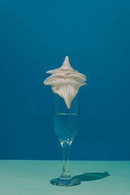 Şampanya bardağında yabani krema. İki tonlu mavi arka plan. Kavramsal küme ve minimalizm.
