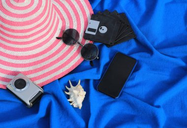 Pembe ve beyaz çizgili şapka, kamera, telefon, güneş gözlüğü, beyaz lavabo ve disketler.