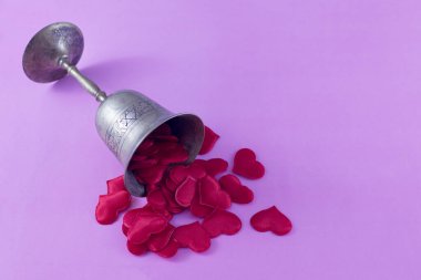 A lying bronze cup and scattered red hearts on a pink background