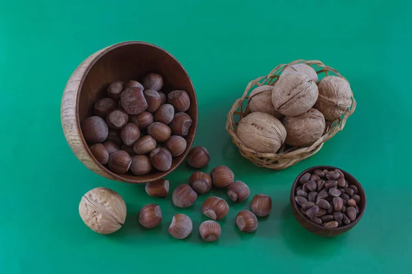 Walnuts, pine nuts in wooden cups, hazelnuts scattered on a green background