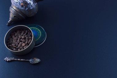 Yuvarlak kavanozdaki kahve çekirdekleri, bir çay kaşığı ve siyah arka planda Türk yağı lambası.
