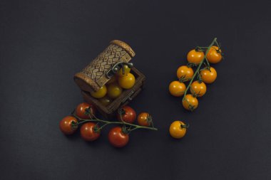 Kırmızı ve sarı domatesler dallarda ve siyah arka planda bir sandıkta