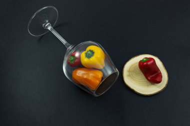 Siyah arka planda yalancı bir şarap kadehinde çok renkli tatlı biberler.