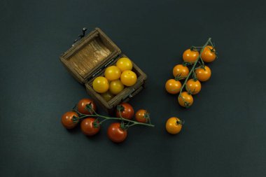 Kırmızı ve sarı domatesler dallarda ve siyah arka planda bir sandıkta