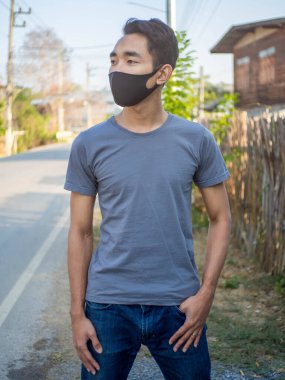 Gri tişörtlü ve maske takan bir adam.