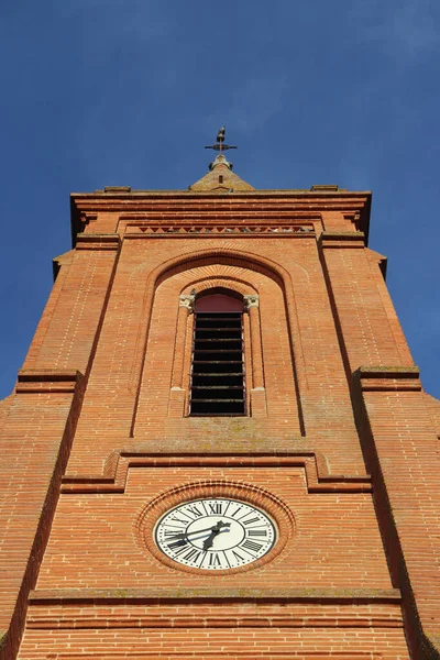 Old clock on the front facade of a red brick medieval church, in the south of France near Toulouse.