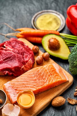 Sağlıklı düşük karbonhidratlı ürünler. Ketogenik diyet. Sığır eti, somon, yumurta, brokoli, domates, fındık, havuç, mantar, salatalık, hurma. Fotokopi alanı olan karanlık bir arka planda diyet yemekleri. Üst Manzara. Düz yatıyordu                               