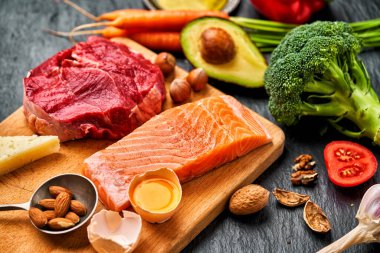 Sağlıklı düşük karbonhidratlı ürünler. Ketogenik diyet. Sığır eti, somon, yumurta, brokoli, domates, fındık, havuç, mantar, salatalık, hurma. Fotokopi alanı olan karanlık bir arka planda diyet yemekleri. Üst Manzara. Düz yatıyordu                               