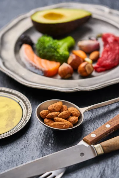 Ketojenik diyet yiyeceğiyle kaplı bir tabak. Sığır eti, somon, yumurta, brokoli, domates, fındık, havuç, mantar, salatalık, hurma. Fotokopi alanı olan koyu arkaplanda diyet yemekleri.                                