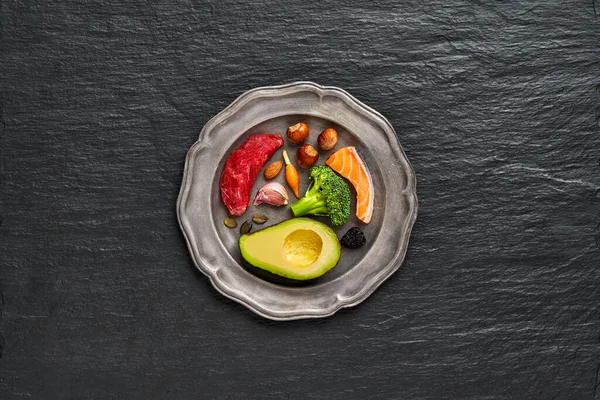 Ketogenic düşük karbonhidrat diyeti, üstten görünüm, metin için yer. Plaka keto gıdalar ile taş siyah arka plan üzerinde: yumurta, et, zeytin yağı, brokoli, meyveler, fındık, tohumlar. Sağlıklı yağlar, kilo kaybı için yeme temiz