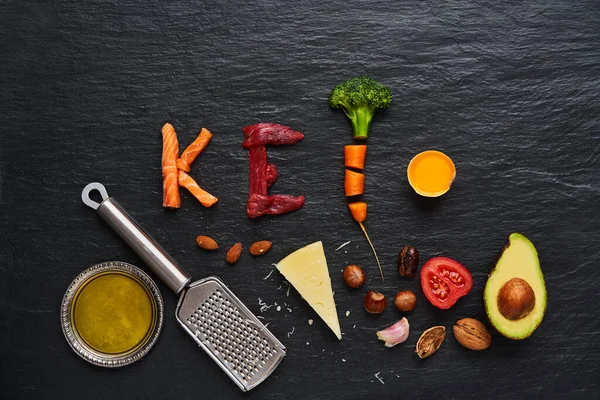  Ketojenik gıdalardan yapılmış keto kelimesi, yeni yıl sağlık diyeti çözeltisi sığır eti, somon, yumurta, brokoli, domates, fındık, havuç, mantar, salatalık, hurma. Fotokopi alanı olan koyu arkaplanda diyet yemekleri.      
