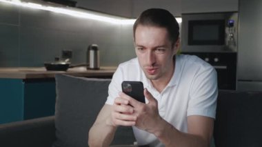 Genç adamın iyi haberler almasına çok şaşırdım. Heyecanlı erkek kazanan akıllı telefona bakarak başarıyı kutluyor ve evde kanepede otururken evet jestleri yapıyor. Mobil zafer kavramı