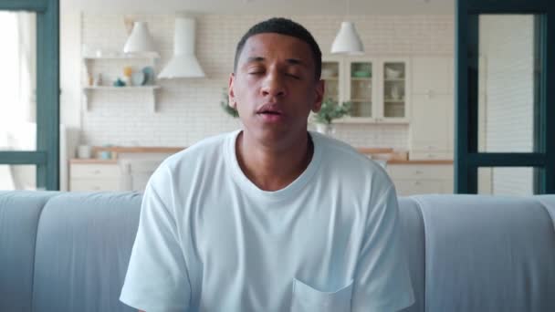Retrato de cerca de un joven afroamericano deprimido, un hombre preocupado sentado en el sofá mirando a la cámara, sintiéndose desesperado, frustrado, agitando la cabeza hacia los lados y mirando hacia abajo — Vídeos de Stock