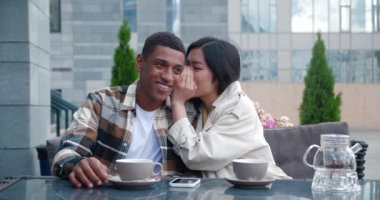 İki güzel çok ırklı insan, yakın arkadaşlar, çok kültürlü, neşeli genç bir çift fısıldaşıyor, fısıldıyor, dedikodu yapıyor, sıcak bir kafeteryanın yaz terasında masada oturuyor.