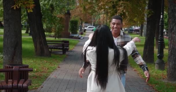 Joven hombre africano alegre y mujer bonita caminando uno hacia el otro, regocijándose en la reunión, abrazándose en el parque, y chico guapo dando vueltas a la chica en sus brazos. Pareja feliz en una cita romántica — Vídeos de Stock