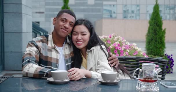 Portrait of two beautiful people, attractive affectionate happy multi-ethnic couple at romantic date, hugging and looking at camera while chilling in the cafeteria on beautiful day. Love, tenderness — Stock Video