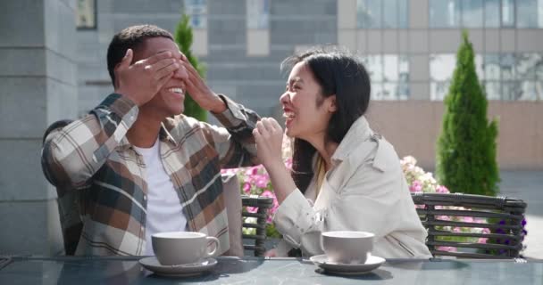 Boldog pár a romantikus randin a szabadtéri kávézó teraszán. Vidám férfi mosolyog fogas mosoly eltakarja a szemét kézzel, míg a felesége barátnője, hogy egy meglepetés, pozitív terhességi teszt — Stock videók