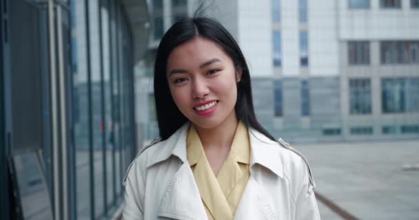 Sonriendo joven hermosa mujer de negocios asiática en ropa formal mira a la cámara afuera en el distrito de negocios. Retrato de chica atractiva al aire libre en las calles de la ciudad. — Vídeos de Stock