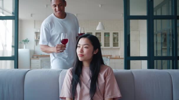 Alegre misto raça afro-americano macho cara foge atrás e trazer um copo com vinho tinto para sua namorada de ascendência asiática, copos de clink com vinho tinto na data, gostando de passar o tempo juntos — Vídeo de Stock