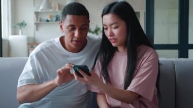 Irklar arası güzel bir çift olan Afro-Amerikalı erkek ve Asyalı kız arkadaşı evdeki kanepede dinlenerek iletişim kuruyor, internetten alışveriş yapıyor, akıllı telefon kullanıyor, gülüyor, tavsiyelerde bulunuyor.